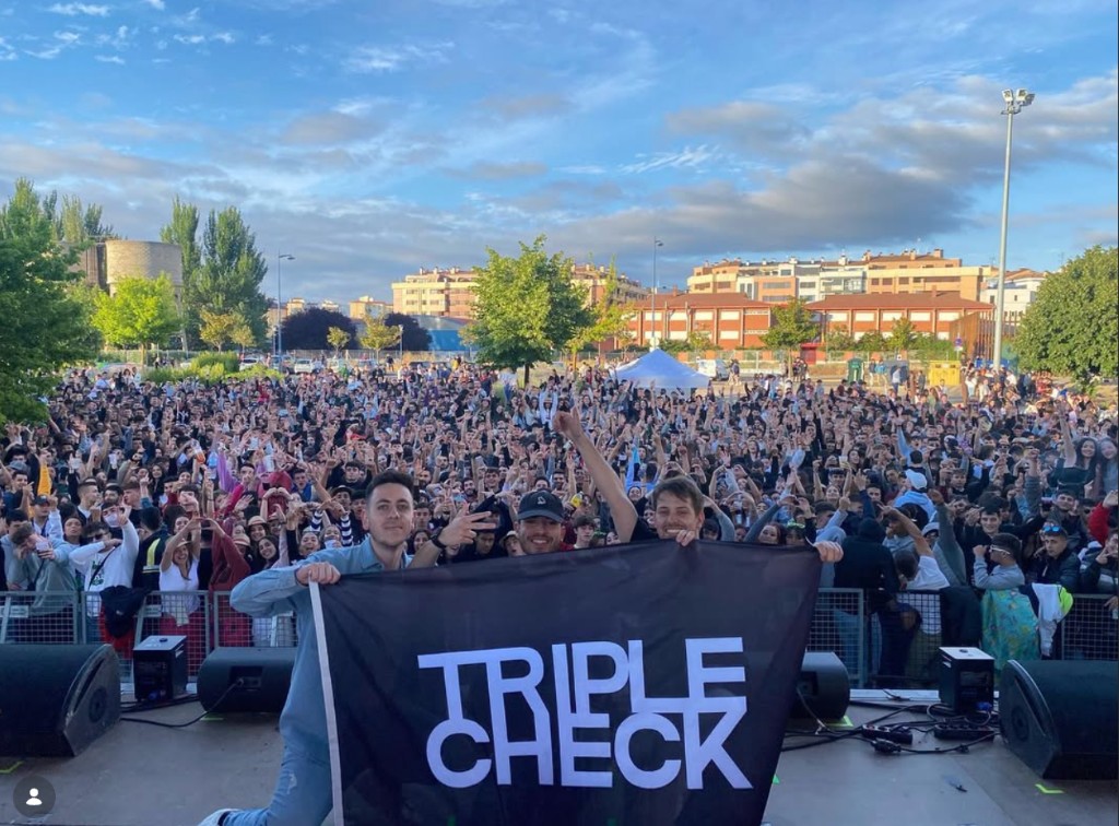 Triple Check — outdoor stage, band holding TRIPLE CHECK banner, large crowd